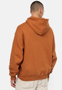 Felpa con cappuccio marrone, dalla vestibilità rilassata, con polsini e orlo a costine e texture morbida. Presenta una singola cucitura sul retro e un cappuccio aderente.