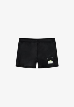 Bañadores negros hechos de una tela suave y elástica. Presentan un parche de logo rectangular en blanco y verde en la parte frontal.