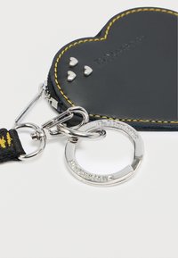 Μαύρο πουγκί σε σχήμα καρδιάς με κίτρινη ραφή, μεταλλικές λεπτομέρειες και ασημένια μεταλλικά μέρη. Διαθέτει φερμουάρ και δακτύλιο για κλειδιά.