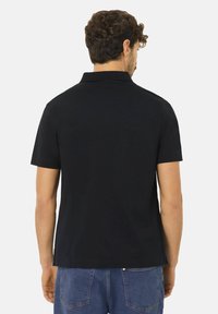 Musta poolo paita lyhyillä hihoilla, jossa on kaulus ja rento leikkaus. Silkkinen puuvillakangas, ilman näkyviä kuvioita tai yksityiskohtia.