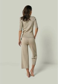 Hellbeiges gestricktes Zweiteiler-Outfit mit einem figurnahen kurzärmeligen Oberteil und weit geschnittenen Hosen, das ein strukturiertes Muster und eine lockere Passform aufweist.
