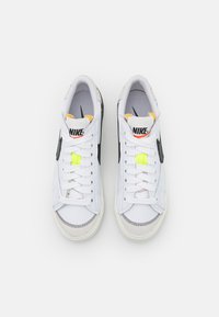 Een paar witte Nike sneakers met zwarte swoosh, witte veters, neon groene vetersluiting en zichtbare gestikte details op de neus.