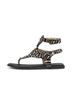 Sandalia plana negra con tiras de rayas de cebra, tachuelas metálicas, hebilla en el tobillo y lazo para el dedo, diseñada para uso casual.