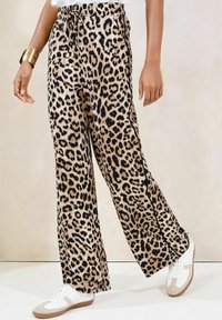 Kalhoty s leopardím vzorem a širokými nohavicemi vyrobené z měkké tkaniny, s elastickým pasem a detailem na šňůrku, doplněné o bílé tenisky.