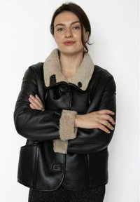 Sort læderjakke med en beige imiteret fåreskinds-krave og manchetter; har matchende knapper og afrundet kant. Tekstureret materiale.