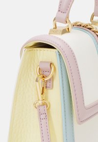 Sac à main bicolore pastel avec côté jaune texturé, panneau bleu clair, bandoulière rose et fermoir en métal doré gravé du nom de la marque.