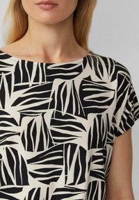 Korte mouwen top met een zwart en crème geometrisch bladerenpatroon, voorzien van een ronde halslijn en zachte, textuurstof.
