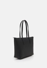 Černá kožená taška přes rameno s two dlouhými uchy a horním zipovým uzávěrem, zobrazená na bílém pozadí.