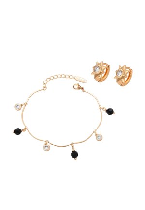 Bransoletka w złotym odcieniu z naprzemiennie ułożonymi czarnymi i przezroczystymi okrągłymi zawieszkami, zestawiona ze złotymi kolczykami w kształcie gwiazdek z przezroczystymi kamieniami.