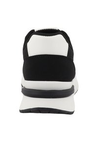 Achteraanzicht van een zwart-witte atletische sneaker met een dikke witte zool en een zwarte buitenzool tegen een witte achtergrond.