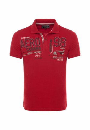 Punane lühikeste varrukatega polosärk kraega, mille esiküljel on trükitud tekstid "AERO," "CARISMA," "98" ja "ADVENTURE".