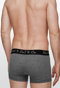 Šedé bavlněné boxerky s černým elastickým pasem s bílým potiskem, viděné ze zadu. Hladká textura a přiléhavý design.