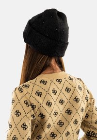 Gorro de punto negro con una superficie texturizada, que presenta pequeños acentos de cuentas. Llevado con un suéter beige que muestra un patrón de diamantes en negro.