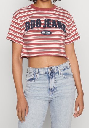 Osoba nosząca krótką koszulkę w czerwono-białe paski z napisem "BDG JEANS Since 1998" oraz jasnoniebieskie dżinsy z wysokim stanem.