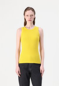 Uten ermer gul ribbestrikket tanktop med rund hals og slim fit. Har et teksturert mønster og subtile sidehull i kanten.