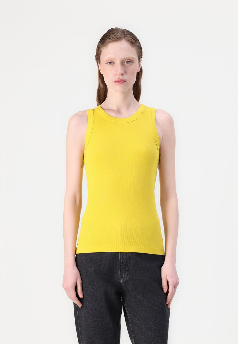 Uten ermer gul ribbestrikket tanktop med rund hals og slim fit. Har et teksturert mønster og subtile sidehull i kanten.