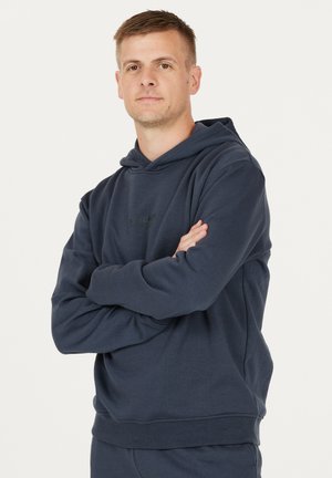 Mørkeblå hættetrøje med en afslappet pasform, lavet af blødt stof. Har en kengurulomme og ribbede manchetter og kant. Minimalistisk logo på fronten.