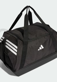 Bolsa de lona negra hecha de tela duradera con diseño de tres franjas blancas y logotipo. Cuenta con asas resistentes y una base estructurada.