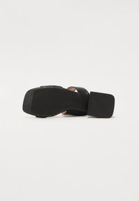 Sandalia negra de tacón alto con una parte superior lisa, una correa gruesa para el tobillo y una suela sólida y texturizada para un mejor agarre. Diseño elegante y contemporáneo.