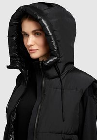 Schwarze Puffer-Weste mit glänzendem, gepolstertem Kapuzenzier, Reißverschluss vorne und Kordelzugdetails. Glatte Textur mit strukturiertem Design und ohne sichtbare Logos.