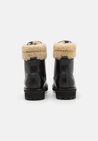 Botas de tobillo de cuero negro con un puño de borrego beige esponjoso. Cuentan con suelas de goma negra gruesa y una lengüeta en la parte posterior.