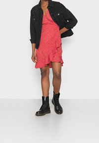 Robe portefeuille rouge à pois avec ourlet à volants, associée à une veste en jean noire et des bottines noires à lacets. Tissu lisse, design décontracté, longueur mi-longue.