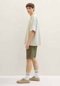 Jasnoszara koszulka z krótkim rękawem w połączeniu z oliwkowymi szortami cargo, białe skarpetki z czarnymi akcentami oraz beżowe trampki. Gładka tekstura materiału.