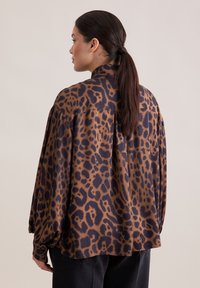 Blusa a stampa leopardata marrone e nera con colletto alto, vestibilità comoda e maniche a sbuffo, realizzata in un tessuto morbido e liscio.
