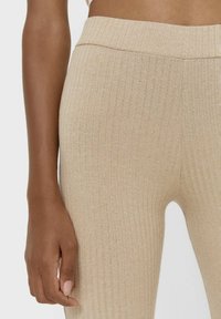 Beige geribde leggings met een elastische tailleband, met een zachte textuur en een figuurvormend ontwerp. Hand geplaatst op de tailleband.