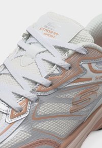 Λευκό και ροδακινί αθλητικό παπούτσι από δίχτυ με κλείσιμο με κορδόνια, σήμα "Stamina Sport" στη γλώσσα και λογότυπο "S" στο πλάι.