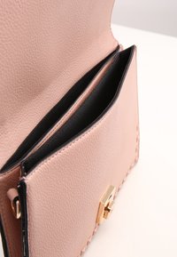 Rektangulär rosa läderhandväska med en texturerad yta, med svart inredning och ett lås i guldfärgad ton. Inkluderar två fack.