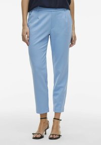 Pantalons taillés bleu clair avec une coupe slim, texture lisse et plis avant. Associés avec des talons noirs avec bride à la cheville.