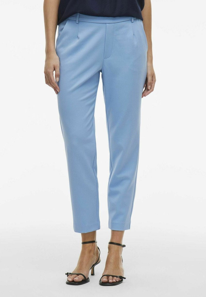 Pantalons taillés bleu clair avec une coupe slim, texture lisse et plis avant. Associés avec des talons noirs avec bride à la cheville.