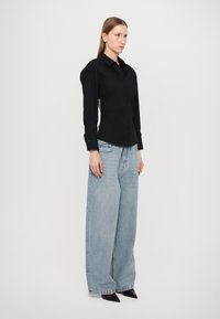 Svart, langermet skjorte med knapper og en tettsittende silhuett, puffede skuldre, kombinert med vide, lyseblå jeans i denim og spisse svarte sko.