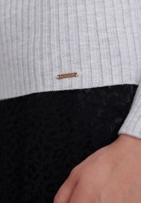 Szary sweter z żeberkowym splotem i czarnym panelem w panterkę na dole. Posiada małą złotą metkę z logo "Superdry."