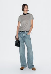 T-shirt grigia a maniche corte abbinata a jeans a gamba larga blu chiaro. Una borsa nera a tracolla e calzature marroni completano l'outfit.