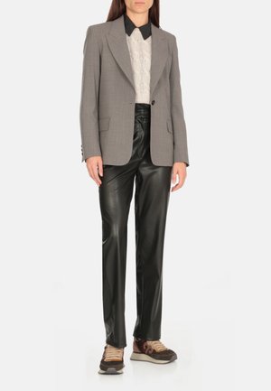 Blazer grigio su misura sopra un pullover bianco a maglia intrecciata, abbinato a pantaloni di pelle neri e sneakers multicolori. Design elegante e strutturato.