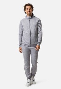 Grauer Zip-Hoodie mit passenden Hosene. Aus strukturiertem Stoff; mit hohem Kragen, Fronttaschen und weißen Akzenten an den Hosen.