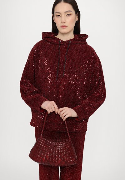 Sequined red hoodie with a drawstring hood, paired with a woven red handbag. The textured outfit features a loose fit and glittering details.
