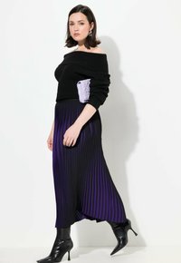 Maglione nero a spalle scoperte abbinato a una maxi gonna plissettata nera e viola. La modella tiene una pochette trapuntata lavanda e indossa stivaletti neri.
