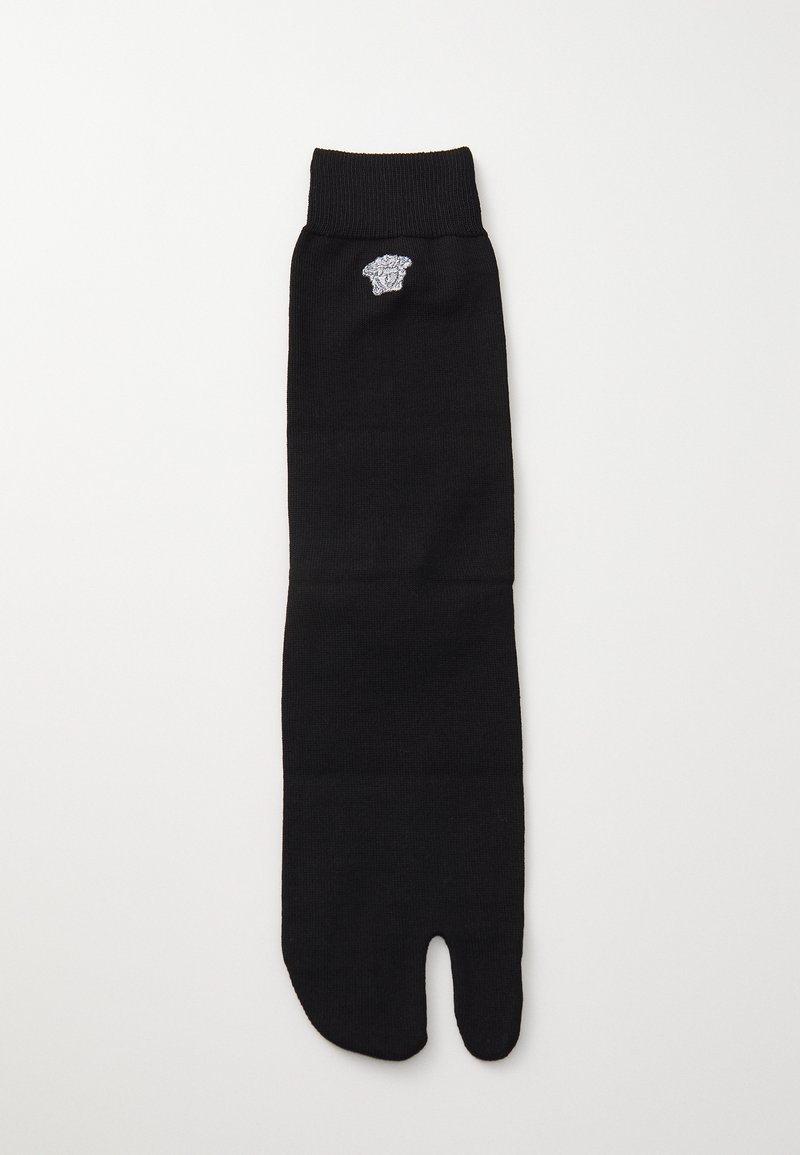 Calcetín negro con diseño de dedo dividido, puño acanalado y pequeño detalle de logo bordado cerca de la parte superior. Fabricado con un material suave y elástico.