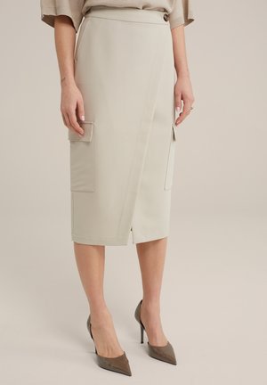 Jupe portefeuille beige en tissu structuré avec poches avant, longueur genoux, présentant une fente latérale et un détail de bouton à la taille.