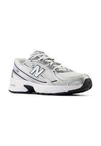 Adidaș alb din material mesh, cu accente gri și talpă din cauciuc negru. Include șireturi, logo pe lateral și un design texturat.