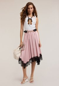 Gonna rosa con orlo in pizzo nero, top smanicato bianco a costine, cintura nera e una borsa chiara. Scarpe bianche con cinturini completano il look.