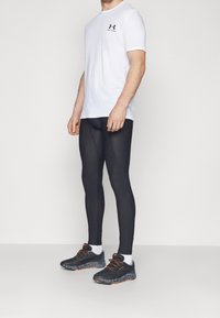 Pánský atletický outfit se skládá z přiléhavého bílého trička s krátkým rukávem, černých přiléhavých legín a černých běžeckých bot s oranžovými akcenty.