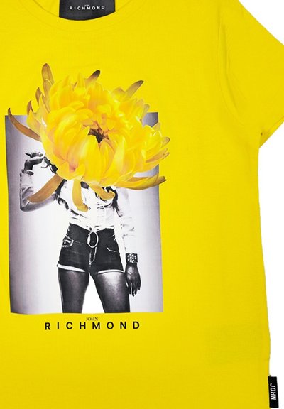 T-shirt di cotone gialla con una grafica di una figura in bianco e nero con pantaloni corti, sovrapposta a un grande motivo di fiore giallo.