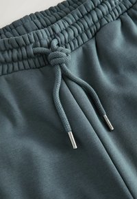 Spodnie dresowe w ciemnym morskim kolorze, z prążkowanym pasem z regulowanym sznurkiem zakończonym srebrnymi metalowymi końcówkami. Miękka tekstura.