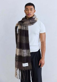Geruite wollen sjaal in donkerbruin en beige, met franjes aan de randen en een wit label met "ARCTIC FOX" merknaam.