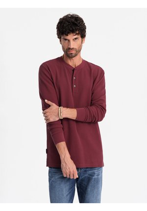 Bordeauxkleurige longsleeve henley shirt met een ronde hals en drie knoopsluitingen. Heeft een gestructureerde stof en een iets getailleerde pasvorm.