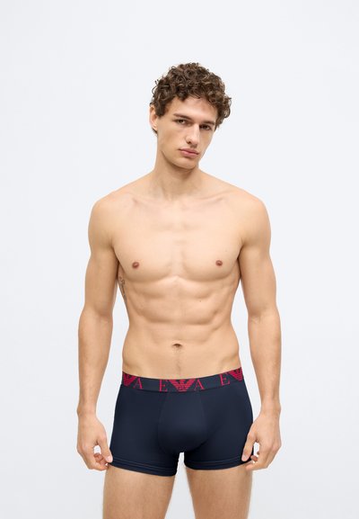 Cuecas boxer azul-marinho com cintura elástica vermelha com logótipo, apresentando um ajuste justo e tecido suave, projetadas para conforto e suporte.